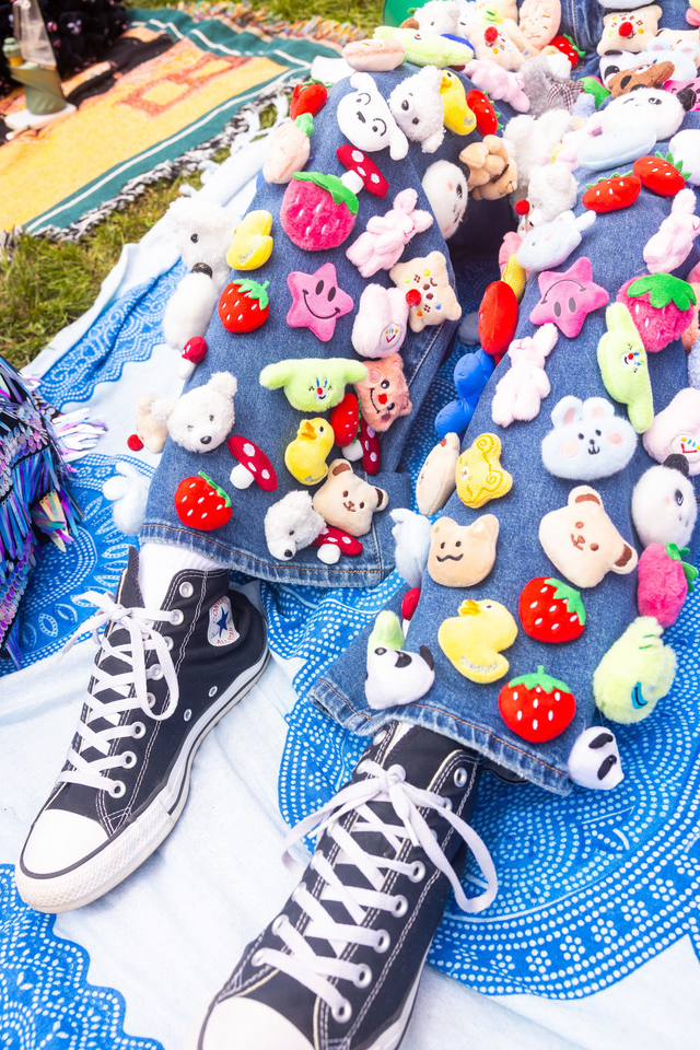 Jeans decorated with colorful felt patches including strawberries, stars, clouds, bears, and other cute shapes cover legs wearing black high-top Converse sneakers.